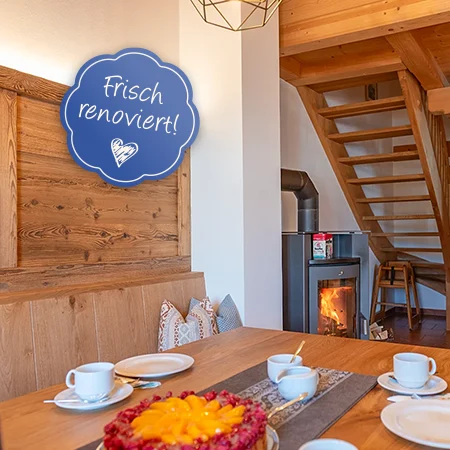 Ferienwohnung Kuckucksnest mit Blick vom mit Kaffee und Kuchen eingedeckten Tisch auf Kaminofen mit Feuer